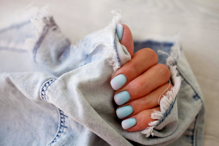 Female hands with a beautiful manicure on a jeans background. Summer trend, blue gradient on the nails with gel polish, shellac . Short nailsの写真素材