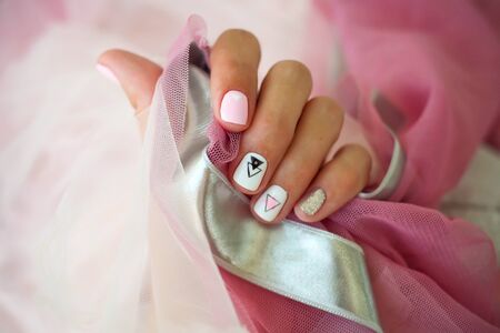 Female hands with a beautiful manicure on a pink background. Summer trend, geometric pattern on nails with gel polish, shellac. Short nailsの写真素材