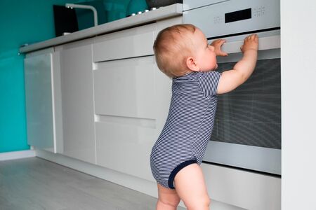 Little child playing with electric stove in the kitchen. Baby safety in kitchenの写真素材