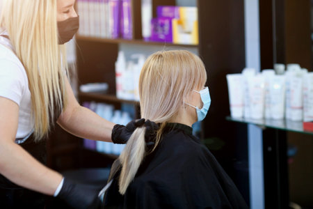 Quarantine period in city is over. A hairdresser in medical mask and rubber gloves holds a pair of...