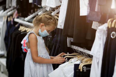 A little girl sits in a cafe in a medical mask and holds a burger and soda in her hands. Opening a cafe. Work cafe with security measures for Covid-19. Work during covid-19 or coronavirusの写真素材