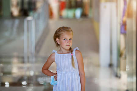 Little Jewish girl holds a medical mask in her hands and looks at the camera. Child stands on blurred shop backgroundの写真素材
