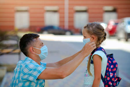 The father puts a surgical masks on his daughter is face. A little girl is going to school during the quarantine period.の写真素材