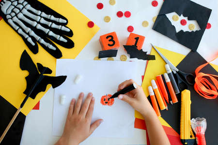 Little girl in a witch costume draws, for the holiday of halloween on a light table.の写真素材