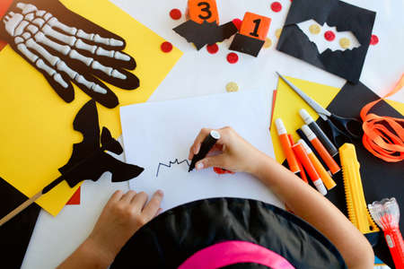 Little girl in a witch costume draw a bat, for the holiday of halloween on a light table. Halloween decor. Handicraft. The concept for Halloween. DIY.の写真素材
