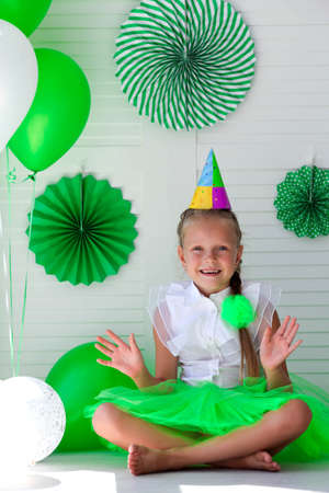 Little girl with a cap on her head against the background of green balloons. Birthday for children. St. Patrick's day celebrationの写真素材