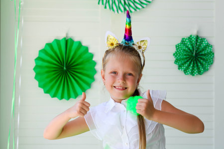 A little girl with a unicorn hoop on her head against a background of green photo decoration....