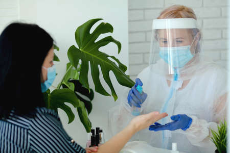 A manicurist in a protective mask and clothes in a beauty salon treats his hands with an antispecialist. Professional procedure. Existence of small businesses in isolation from COVID-19.の写真素材