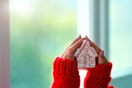Women is hands in a red sweater are holding a Christmas toy in the shape of a house. Stay home. Copy...