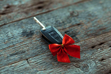 Car key with a red ribbon bow on a wooden background. Gift for Christmas or Valentine is Day or present an abstract concept.の写真素材