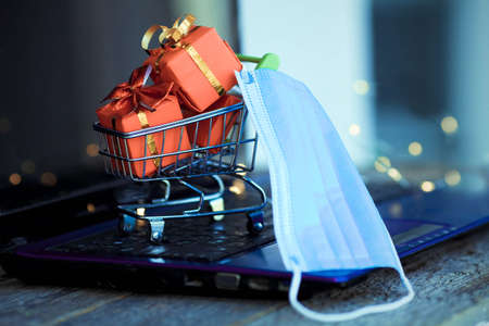 Small basket with boxes of Christmas gifts and a medical mask on the background of a laptop. Online shopping. Boxing day concept in the COVID-19 pandemic. Manage to buy. Sales.の写真素材