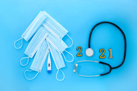 Christmas tree made of medical masks and a thermometer and a stethoscope with the numbers 2021 on a blue background. The concept of Christmas ahead of the COVID-19 pandemicの写真素材