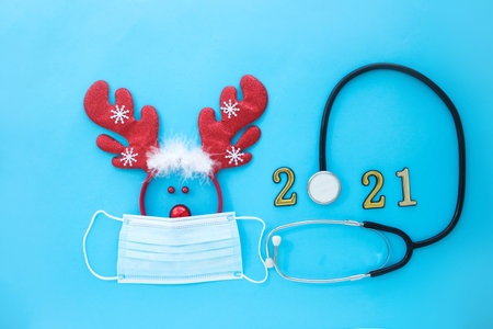 Deer antlers in a medical mask and stethoscope with numbers 2021 a on a blue background. Christmas concept during COVID-19 pandemicの写真素材