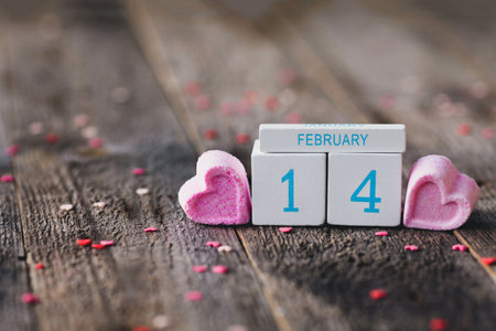 Date of February 14 on wood calendar and pink hearts on the sides on wooden background. Copy space. Valentine's Day.の写真素材