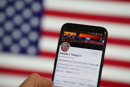 Krasnodar, Russia January 10, 2021. A man's hand holds a smartphone with Donald Trump is Twitter page on the background of the American flag. President Trump is blocked Twitter account on mobileのeditorial素材