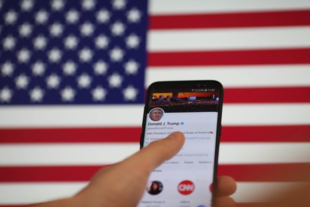 Krasnodar, Russia January 10, 2021. A man's hand holds a smartphone with Donald Trump is Twitter page on the background of the American flag. President Trump is blocked Twitter account on mobileのeditorial素材