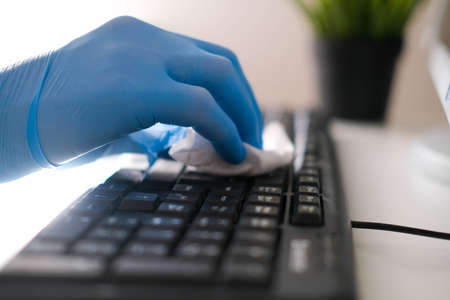 Male hands in rubber gloves wipe the keyboard from the computer. Disinfection in the office during COVID-19の写真素材