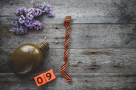 Flask, george ribbon and lilacs on a wooden background. Wooden calendar with date 9 May. Victory...