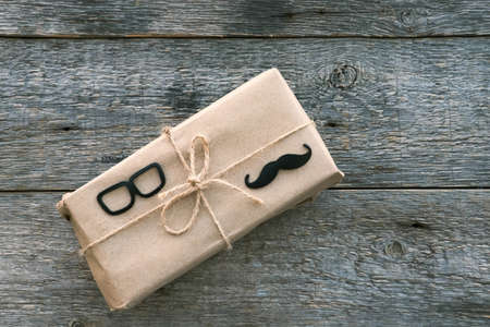 Happy Fathers Day concept. Gift box wrapped craft paper black glasses and mustache sign on the wooden background. Fathers Day sale promotion poster design Blank copy space for lettering.の写真素材