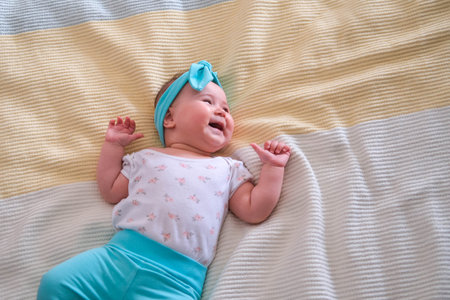 The baby is 6 months old and lies on the bed and smiles. A beautiful headband for a baby. Copy space.の写真素材