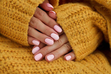 Female hands with beautiful oval-shaped nails, matte pink manicure close-up on a knitted sweater background. Shellac. Copy spaceの写真素材