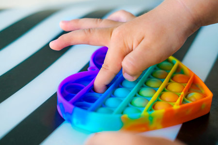 Child playing with rainbow pop it fidget toy. Push bubble fidget sensory toy - washable and reusable silicon stress relief toy. Antistress toy for child with special needs.の写真素材