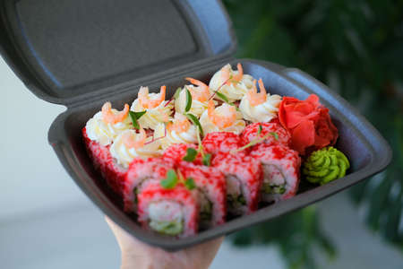 Hand holds a cork with a set of sushi and rolls decorated with microgreens. Food delivery. California rolls with shrimp.の写真素材