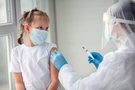 Doctor is hands in rubber gloves makes a shot in the shoulder of a child in a medical mask....