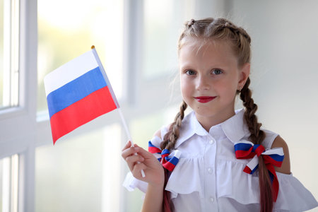 School child stands and holds the flag of Russia. Little girl with face painting of Russian symbolism. Russian flag day.の写真素材