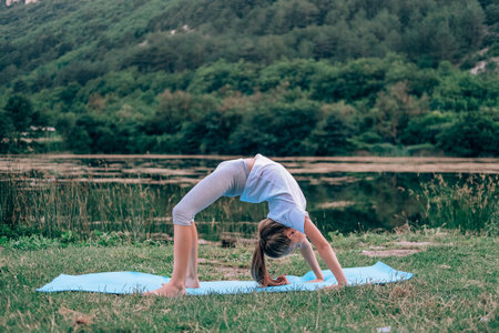 A little girl makes a bridge, bending her back in nature. A flexible child, doing gymnastics exercises. Sports, learning, fitness, stretching, yoga, active lifestyle conceptsの写真素材