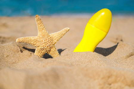 Spray with sunscreen and starfish on the beach. Summer, sea, vacation, sun protection.の写真素材
