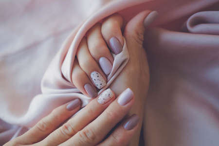 Women - hands with beautiful manicure on a background of silk fabric. Autumn trend, polish the beige and quail pattern on the nails with gel polish, shellac. Copy space.の写真素材