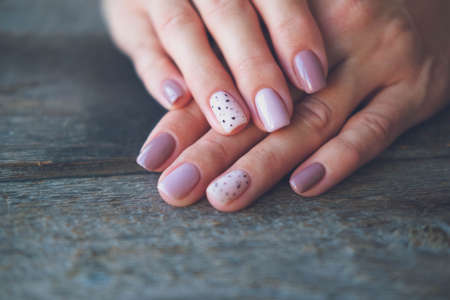 Women is hands with a beautiful manicure on a wooden background. Autumn trend, polish the beige and quail egg pattern on the nails with gel polish, shellac. Copy space.の写真素材