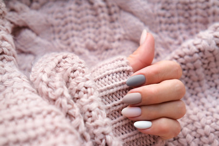 Women's hands with a beautiful matte oval manicure in a warm knitted sweater. Winter trend, polish beige nails with gel polish, shellac. Copy space.の写真素材