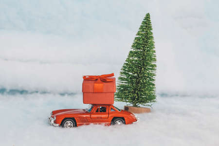 Krasnodar, Russia - December 10, 2019: Red toy car with a gift on the roof, rides in the snow. Delivery of gifts. Copy space. Christmas. New year.の写真素材