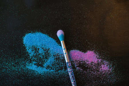 Makeup brush and shiny pink and blue sequins on a black background. Festive magic makeup concept. Template for design, top view Flat Lay Copy space.の写真素材