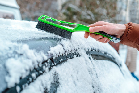 A man holds a brush in his hands and cleans the windows of the car from snow. The concept of...