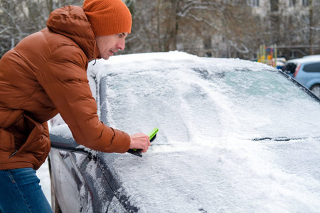 A man holds a brush in his hands and cleans the windows of the car from snow. The concept of...