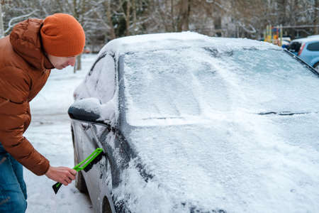 A man holds a brush in his hands and cleans the windows of the car from snow. The concept of transport, winter, weather, people and vehicles.の写真素材