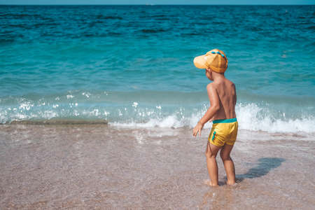 A little boy in a headdress looks at the sea. A child in a cap stands on the beach with his back. Summer holiday concept. summertime. Travel.の写真素材