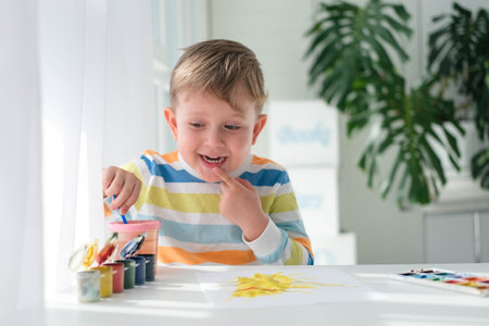 Happy kid painting with brush and colorful paints. A little boy draws a picture with paints on a sheet of paper. The child is learning to draw. home creativity.の写真素材