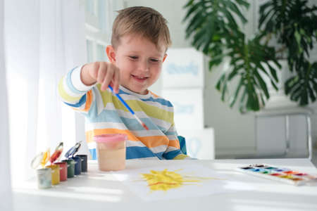 Happy kid painting with brush and colorful paints. A little boy draws a picture with paints on a sheet of paper. The child is learning to draw. home creativity.の写真素材