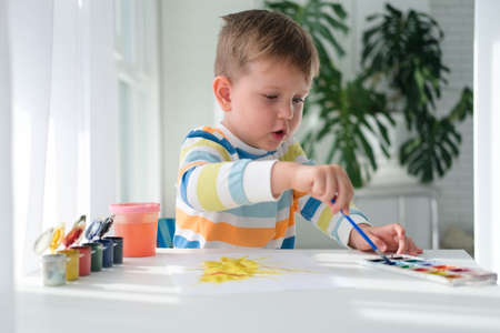 A little boy draws a picture with paints on a sheet of paper. The child is learning to draw. home creativity.の写真素材