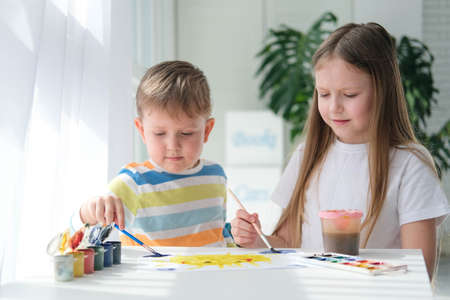 Brother and sister draw a picture with paints on a piece of paper. Children are learning to draw. home creativity.の写真素材