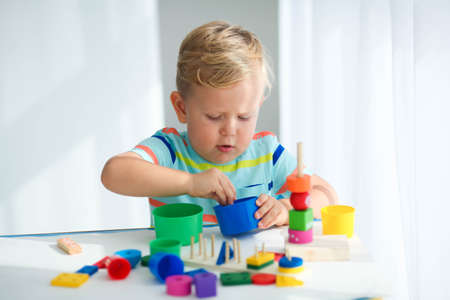 A little boy plays with wooden toys and builds a tower. Educational logic toys for children. Montessori games for child development. Children's wooden toy.の写真素材