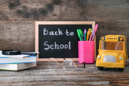 School board with the inscription back to school and a stack of books on a wooden background. Glasses for vision correction. School concept: books, pens, pencils and school bus.の写真素材