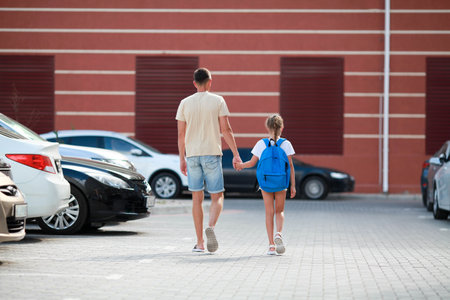 The father takes his daughter to school. A dad and his little girl go to school through the laundry room. A child with a briefcase on his back.の写真素材