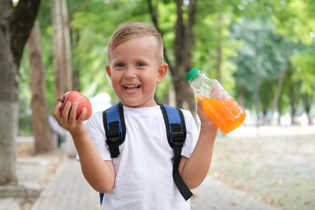 Little boy eats an apple and drinks juice. A child with a backpack looks at the camera and laughs.の写真素材