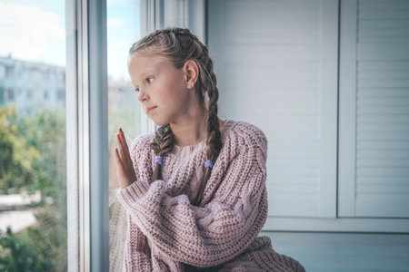 A sad girl is sitting near the window in a knitted sweater. autumn melancholy.の写真素材