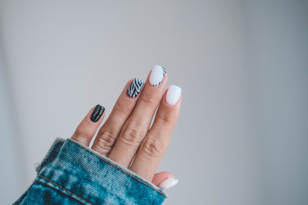 Beautiful female hands with a manicure in a denim jacket. Stylish nail designs. Manicure with black and white zebra stripes on the nails.の写真素材